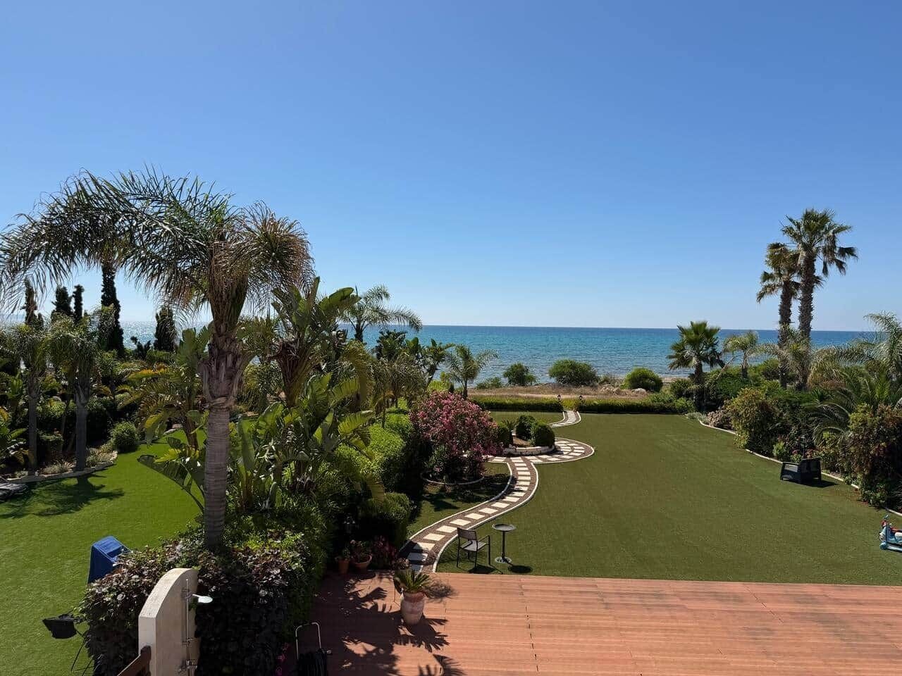 Un jardín ajardinado con un sendero curvo, palmeras y vista al mar.