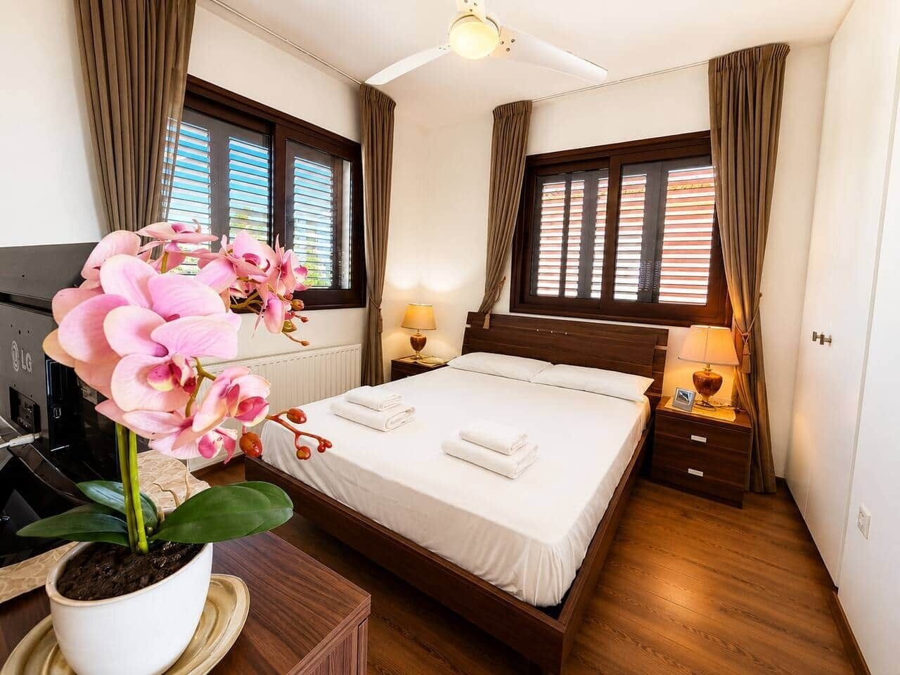 A hotel room with a bed, bedside tables, a ceiling fan, and a potted orchid.