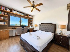 A bedroom with a large bed, a desk with a chair, a bookshelf, and a view of the outdoors. - Emerald Seafront Residence (Sotira)
