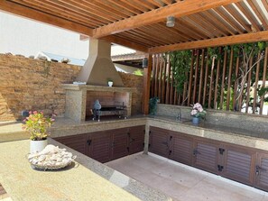 An outdoor kitchen area with a stone countertop, a grill, and a seating area. - Emerald Seafront Residence (Sotira)