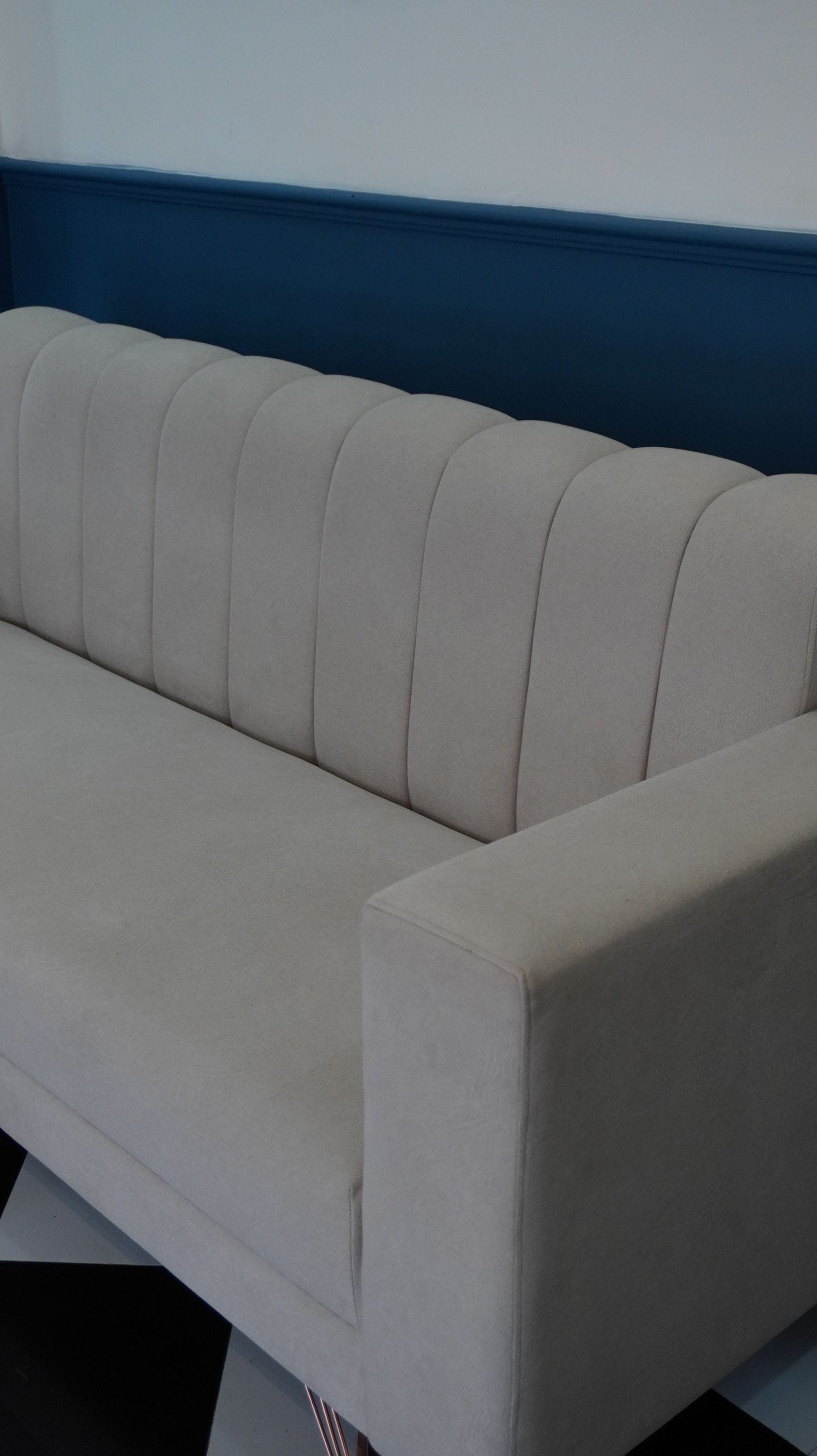 A sofa with a straight backrest and a curved armrest, positioned against a wall with a blue trim.