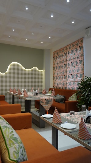Un restaurante con paredes de cuadros, un tapiz estampado y asientos tapizados en naranja.
