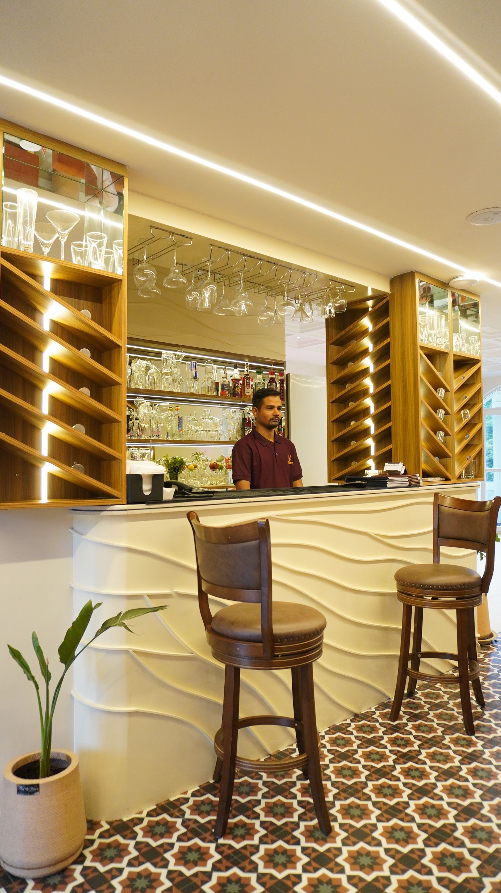 A bar area with a counter, bar stools, and shelves with glassware.
