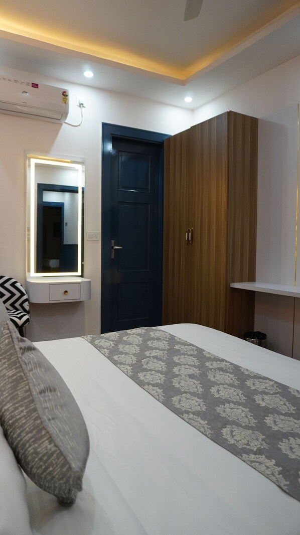 Une chambre à coucher avec un lit, une armoire, un miroir avec éclairage et une porte.