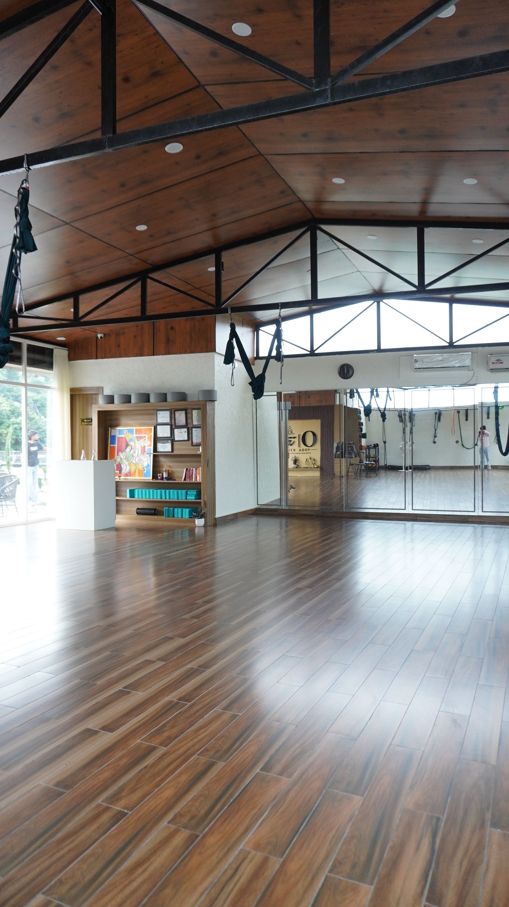 A spacious indoor area with a wooden floor, a reception desk, and a wall with hanging exercise equipment.