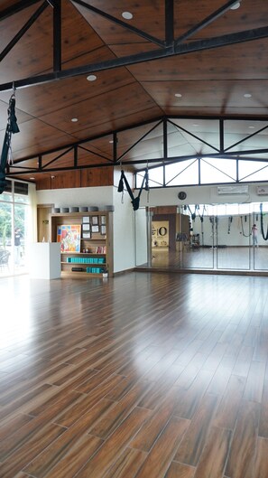A spacious indoor area with a wooden floor, a reception desk, and a wall with hanging exercise equipment. - Macpro Inn Rubystone Express  (Dehradun)
