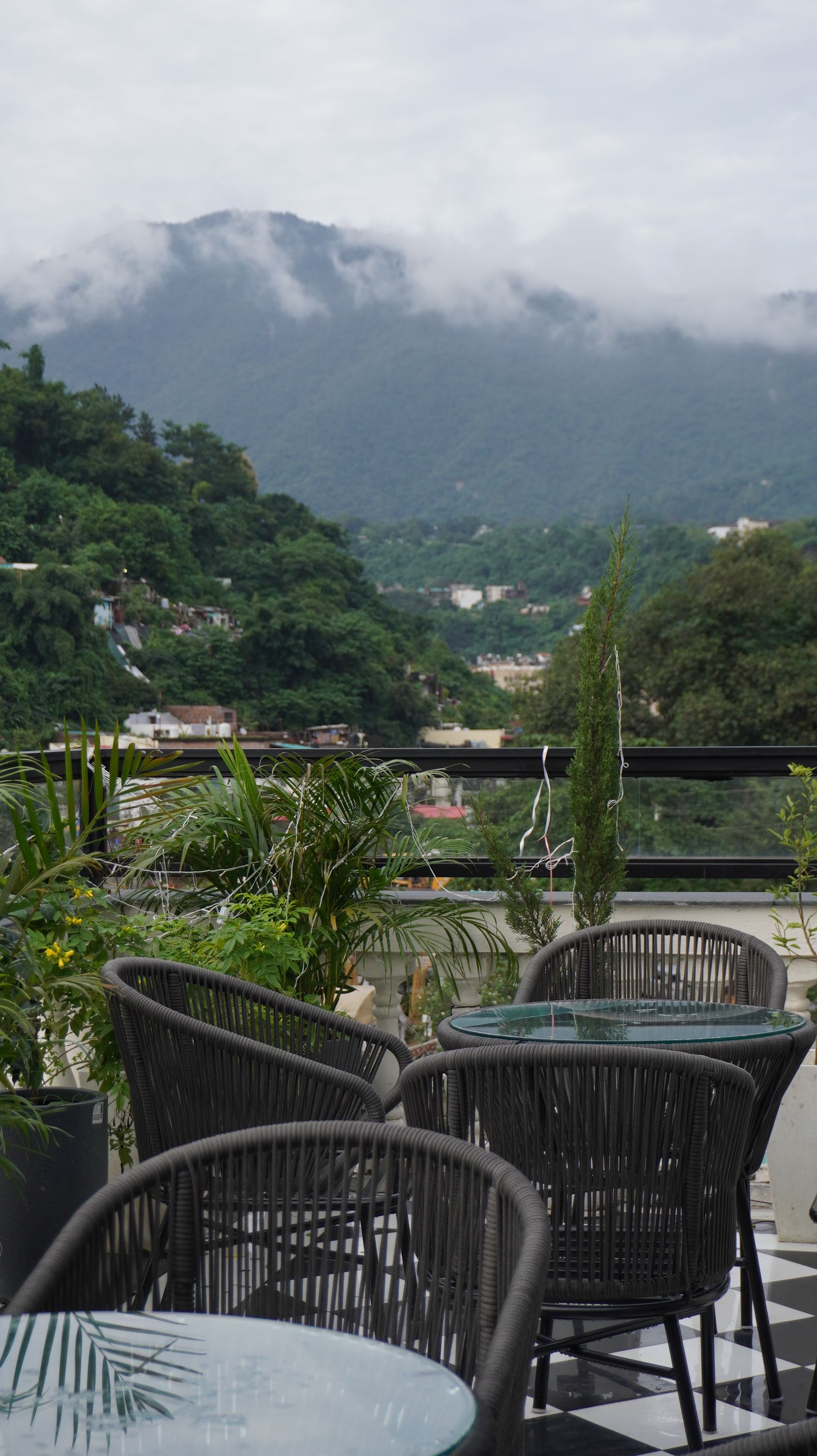 Sillas de mimbre exteriores y una mesa de vidrio en una terraza con vista a un paisaje montañoso.