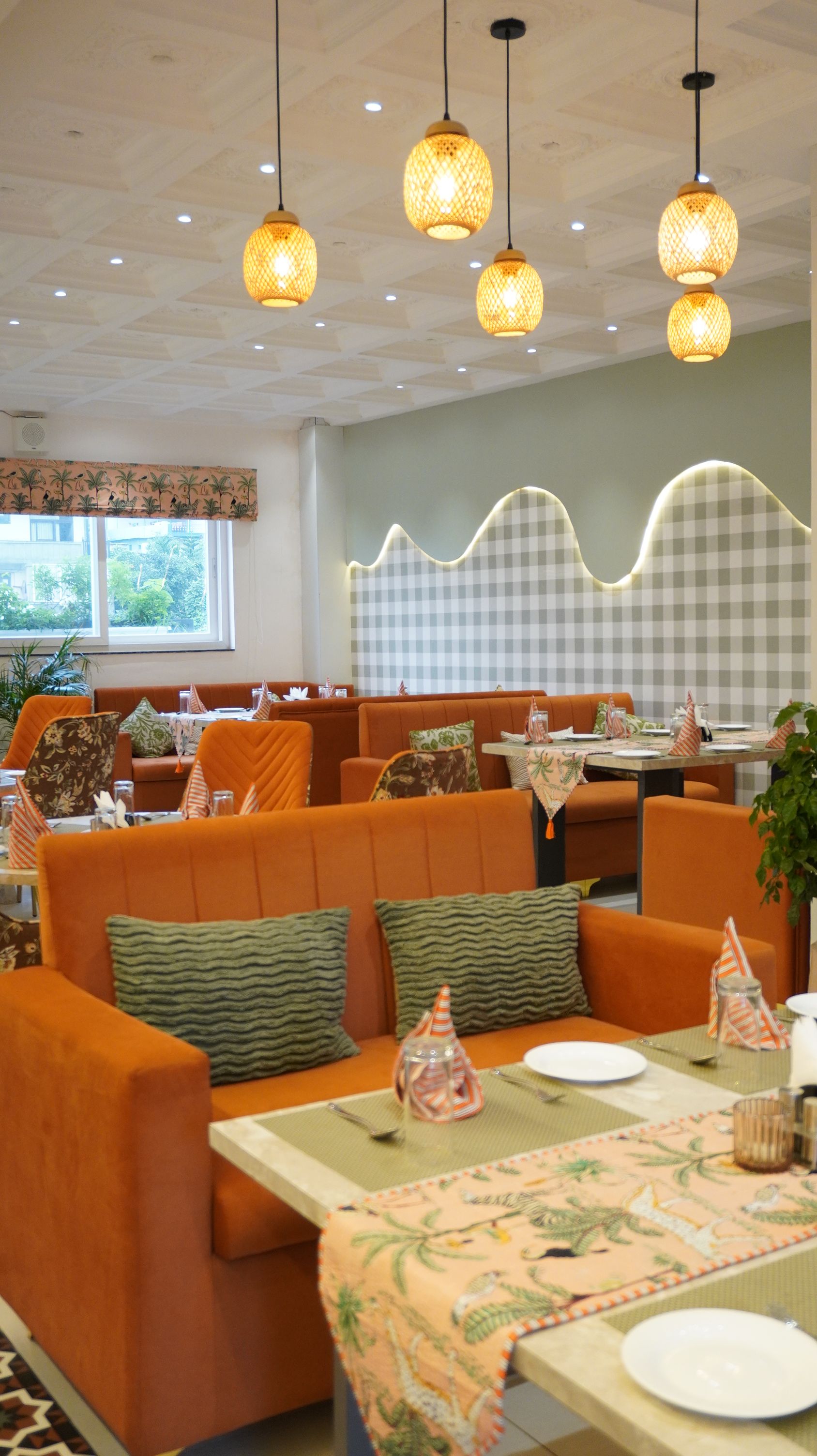 A restaurant with orange seating, checkered wall patterns, and hanging lamps.