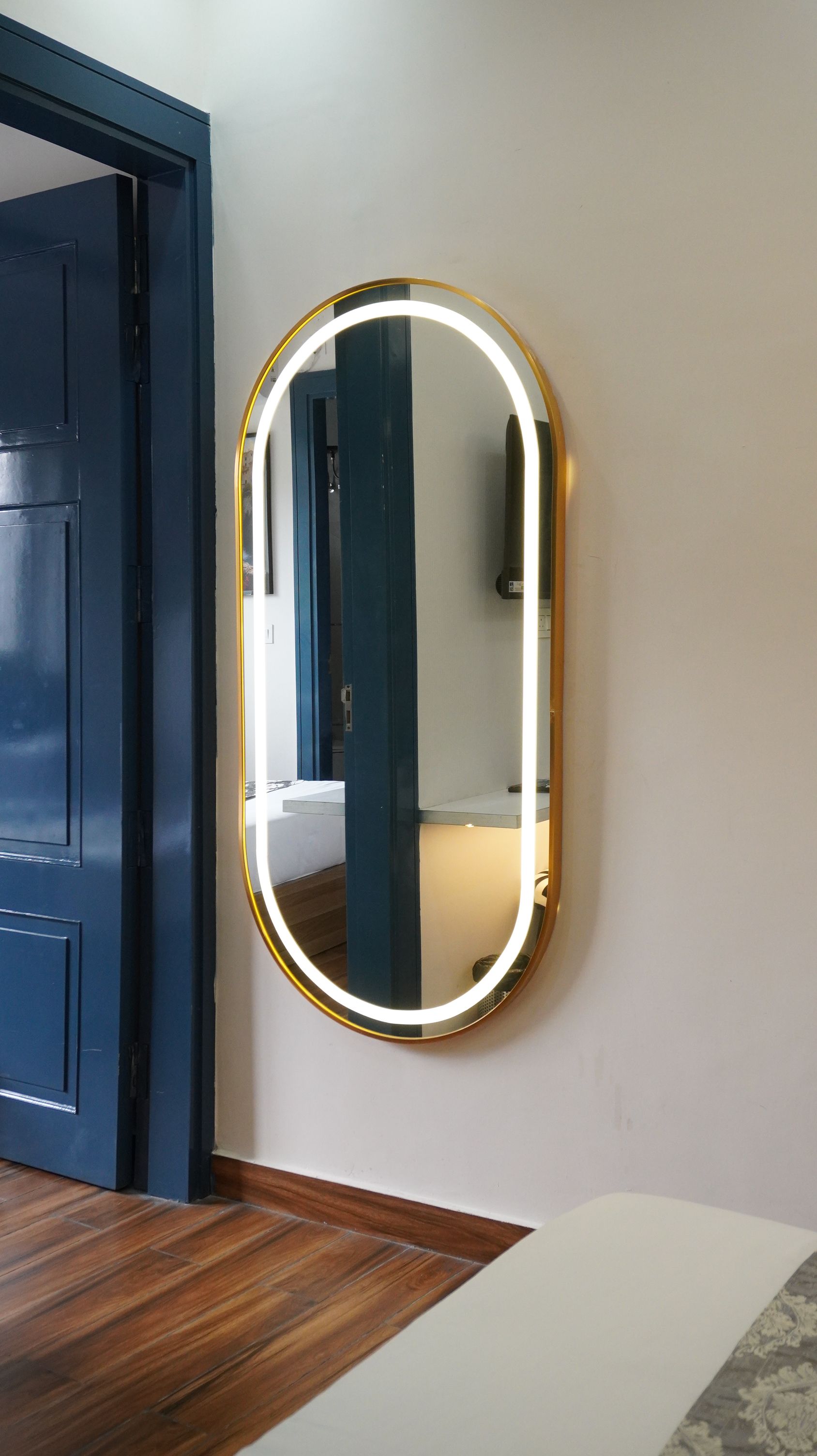 Una habitación con una puerta, un espejo con luz instalado en la pared y suelo de madera.