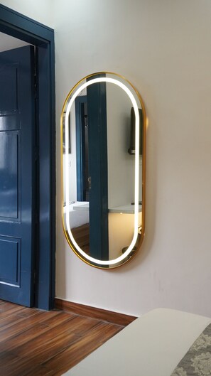 A room with a door, a wall-mounted mirror with a light, and a wooden floor. - Macpro Inn Rubystone Express  (Dehradun)