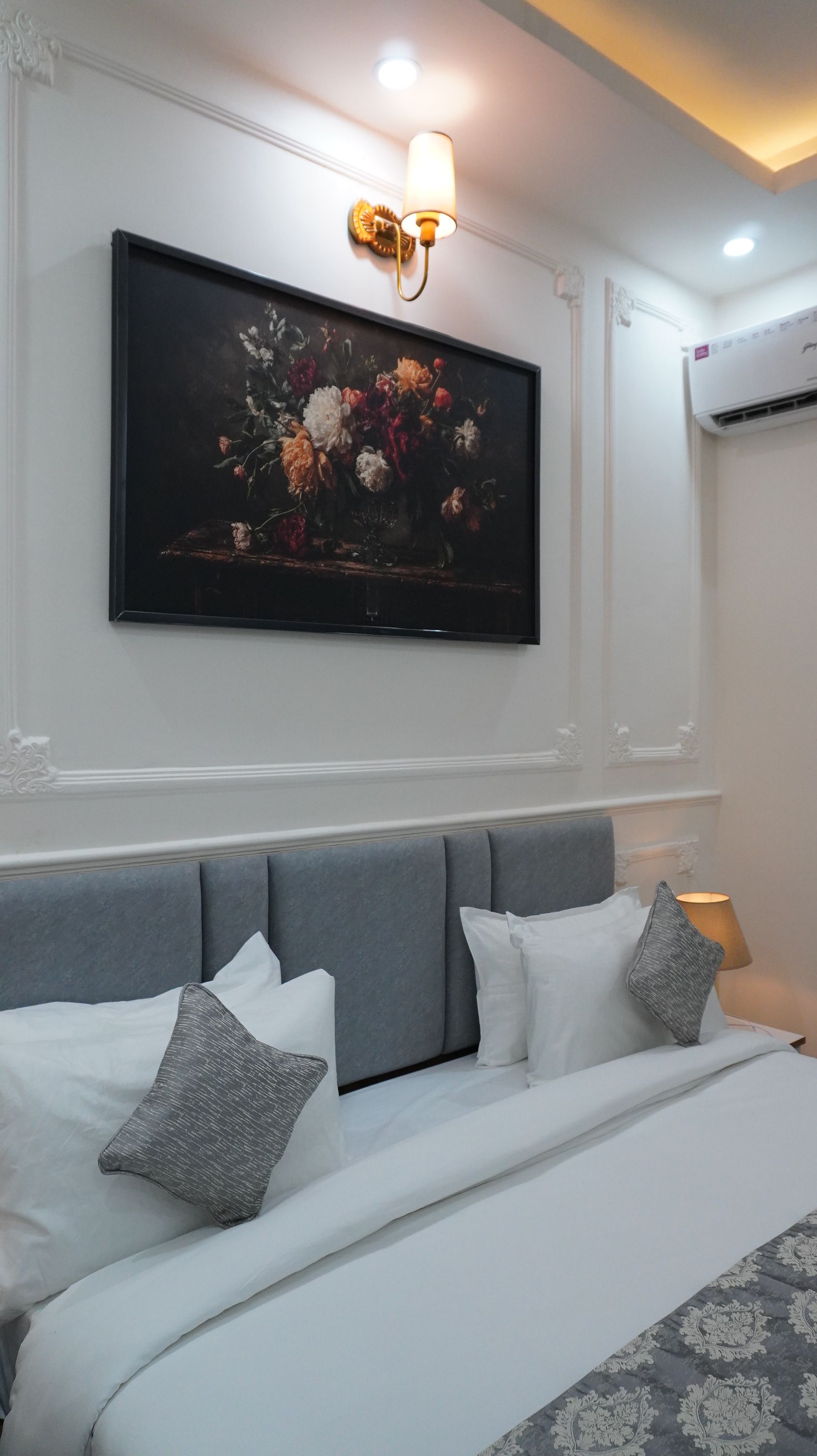 Una camera da letto con un letto, cuscini, un quadro appeso al muro e un lampadario.