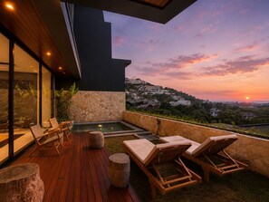 A modern outdoor deck with a pool, lounge chairs, and a view of a hillside town during sunset. - Villa Elora - Bingin Pecatu (Pecatu)