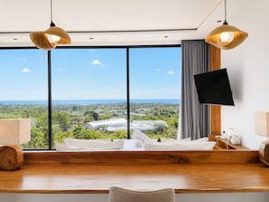 A modern room with a large window, a bed, a wooden desk, and a flat-screen TV mounted on the wall. - Villa Elora - Bingin Pecatu (Pecatu)
