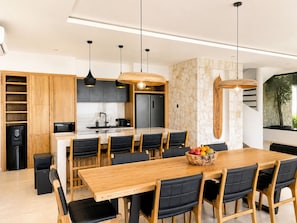 A modern kitchen with a central island, black chairs, and a wooden dining table with a fruit bowl. - Villa Elora - Bingin Pecatu (Pecatu)