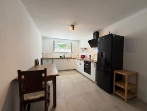 Une cuisine compacte avec une table à manger, un réfrigérateur noir et un petit tabouret en bois.
