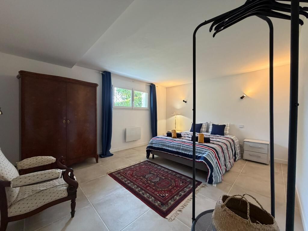 Un dormitorio con cama, una silla, un armario y una ventana.