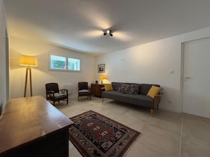 Ein Wohnzimmer mit einer Couch, zwei Sesseln, einem Holztisch, einem gemusterten Teppich und einem Deckenventilator.