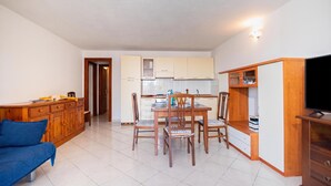 A compact living space with a dining area, kitchenette, and a television on a wooden stand. - Il Rifugio Di Daniela (San Teodoro)