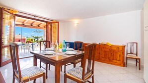 A dining area with a wooden table set for four, chairs with cushioned seats, and a view of a garden through an open door. - Il Rifugio Di Daniela (San Teodoro)
