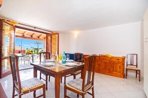 Ein Essbereich mit einem Holztisch, gedeckt für vier Personen, Stühle mit gepolsterten Sitzen und Blick auf einen Garten durch eine offene Tür.