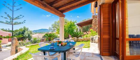 A covered outdoor seating area with a table and chairs, stone flooring, and a view of the surrounding landscape.