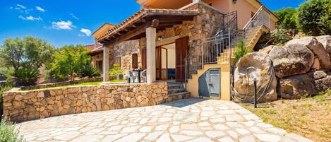 A house with a stone facade, a stone patio, and a staircase leading to a covered porch.