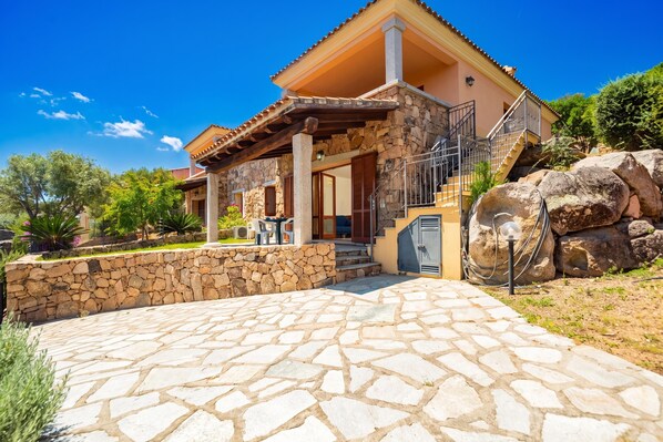 Une maison avec une façade en pierre, un patio en pierre et un escalier menant à un porche couvert.