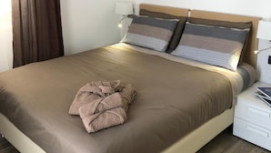 Una cama bien tendida con una manta marrón y almohadas, un adorno de pared y una mesita de noche con una lámpara.