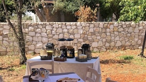Mesa de comedor al aire libre con platos, cubiertos y comida, rodeada de muros de piedra y árboles.