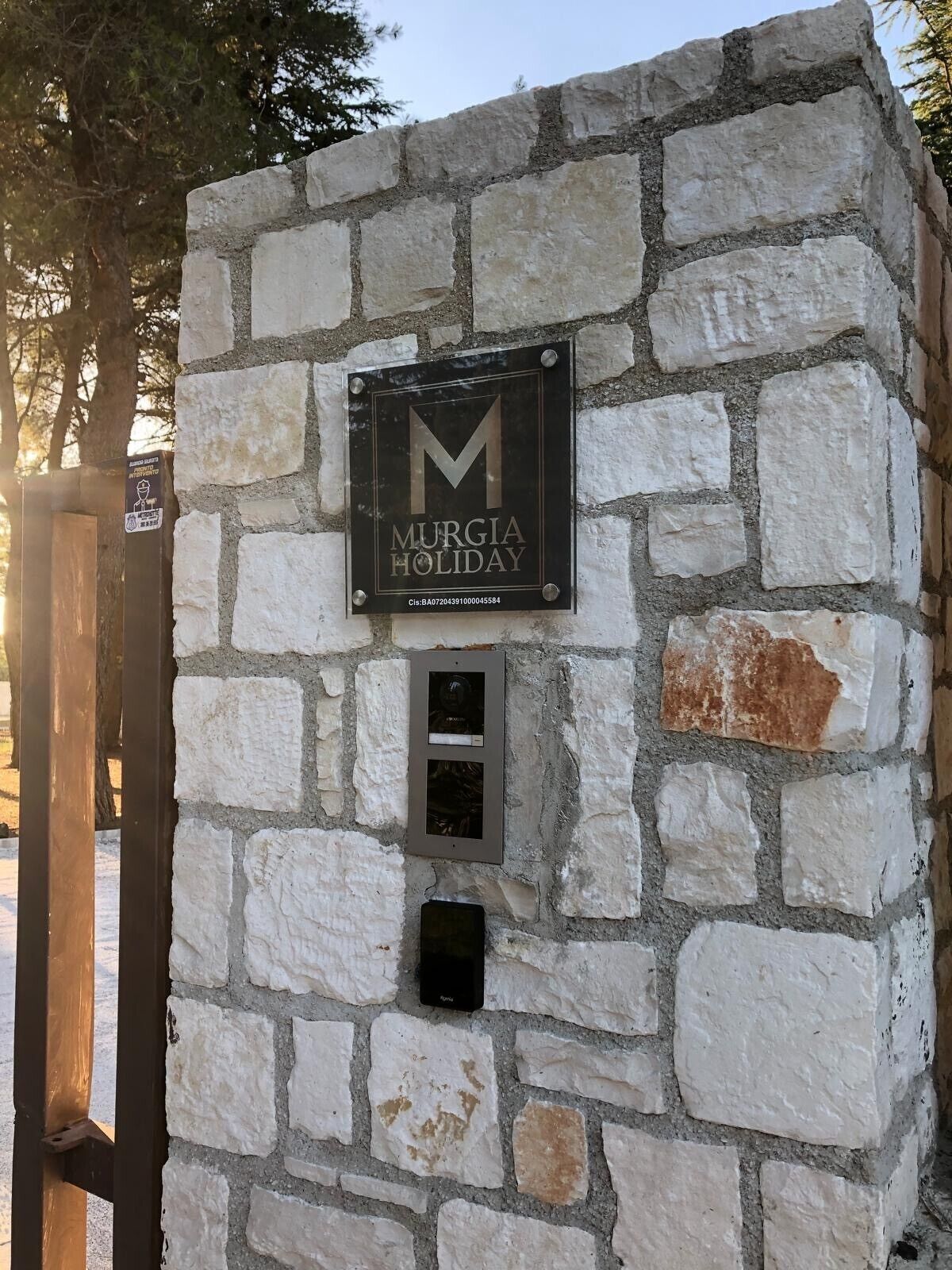 A stone wall with a sign for 'MURGIA HOLIDAY' and a metal intercom.