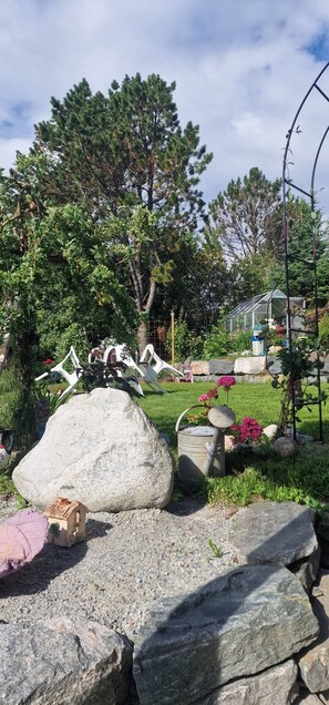 A garden with large rocks, a small house model, and a greenhouse.