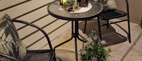 Un espacio al aire libre con dos sillas, una mesa, un farol y una planta en maceta.