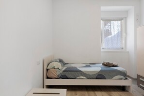Ein kleines Zimmer mit einem Einzelbett, einem Fenster, einem Nachttisch und einem Kleiderschrank.