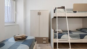 Een slaapkamer met stapelbed, een kast, een raam met gordijnen en een bed met dekbed.