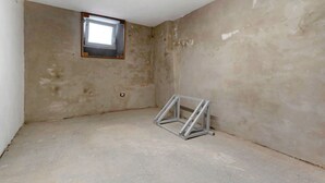 Een kamer met onafgewerkte muren, een klein raam en een metalen constructie op de vloer.