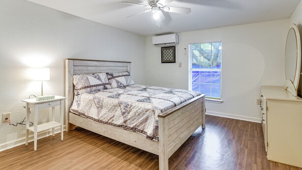 Een slaapkamer met een bed, nachtkastje met lamp, plafondventilator, airconditioning en een raam met zonwering, plus een dressoir.