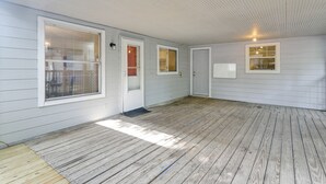 Een overdekte veranda met houten vloer, witte buitenmuren en meerdere ramen met zonwering.