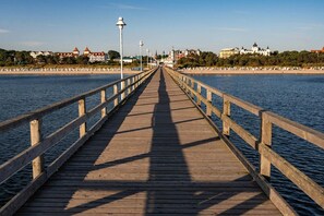 A wooden pier extending into calm water, with buildings and a clear sky in the background. - Holtz 3 Vacation Rental with a Balcony, Parking, and a Garden with a Grill - (Zinnowitz)