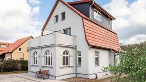 A two-story residential building with a red-tiled roof, white exterior walls, and a small front garden with a bench. - Holtz 1 Vacation Rental with a barbecue area in the garden and a lawn for sunbathing - Dogs are (Zinnowitz)