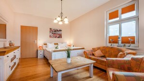 A cozy living room with a wooden floor, a white sofa, a patterned armchair, a coffee table, and a painting on the wall. - Holtz 1 Vacation Rental with a barbecue area in the garden and a lawn for sunbathing - Dogs are (Zinnowitz)