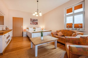 Ein gemütliches Wohnzimmer mit Holzboden, einem weißen Sofa, einem gemusterten Sessel, einem Couchtisch und einem Bild an der Wand.