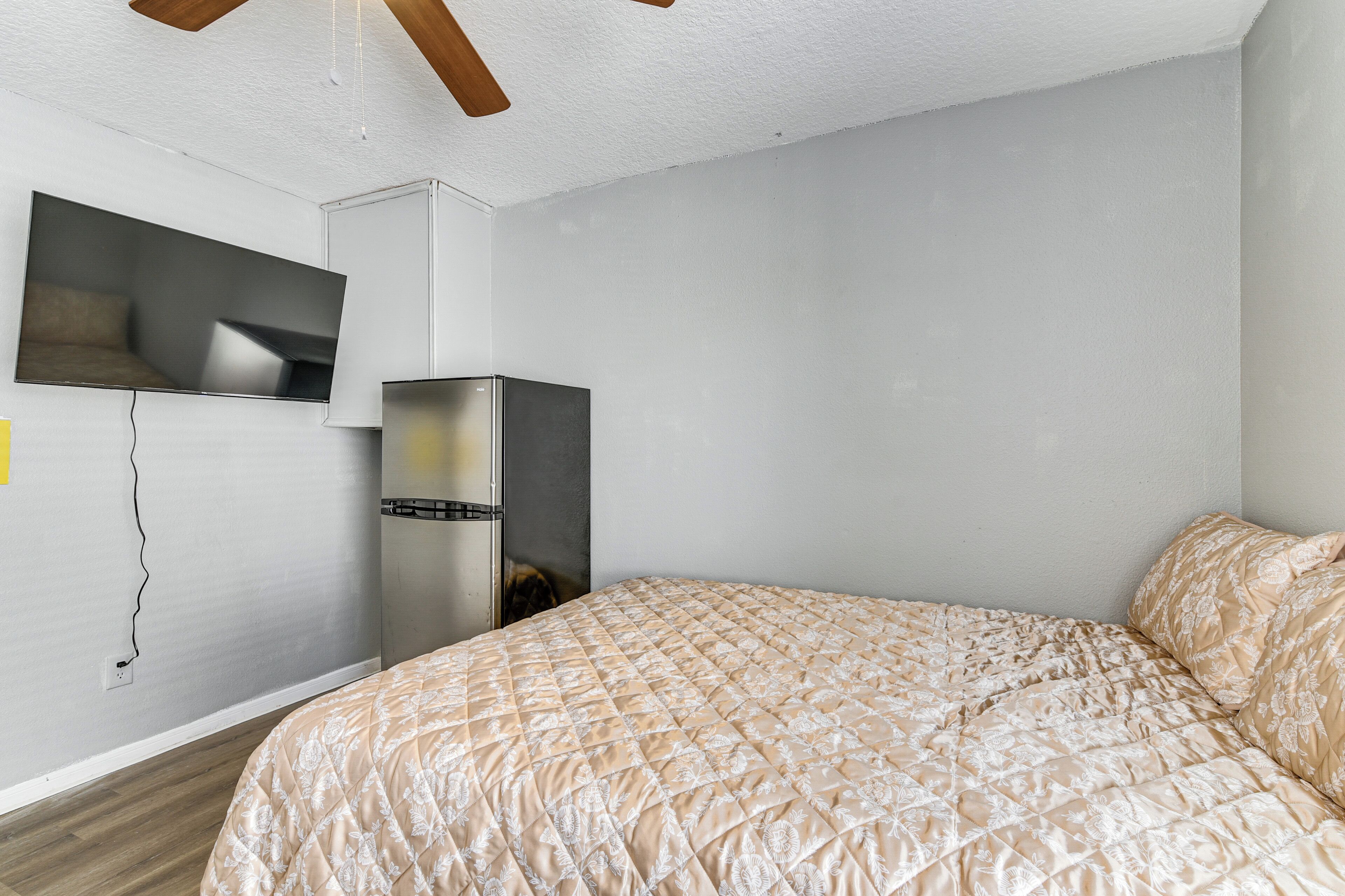 Ein Schlafzimmer mit einem Bett, einem an der Wand montierten Fernseher und einem Kühlschrank.
