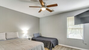 Ein Schlafzimmer mit Bett, Nachttisch, Schreibtisch, Deckenventilator und einem Fenster mit Jalousien.