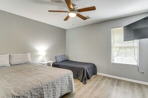 Ein Schlafzimmer mit Bett, Nachttisch, Schreibtisch, Deckenventilator und einem Fenster mit Jalousien.