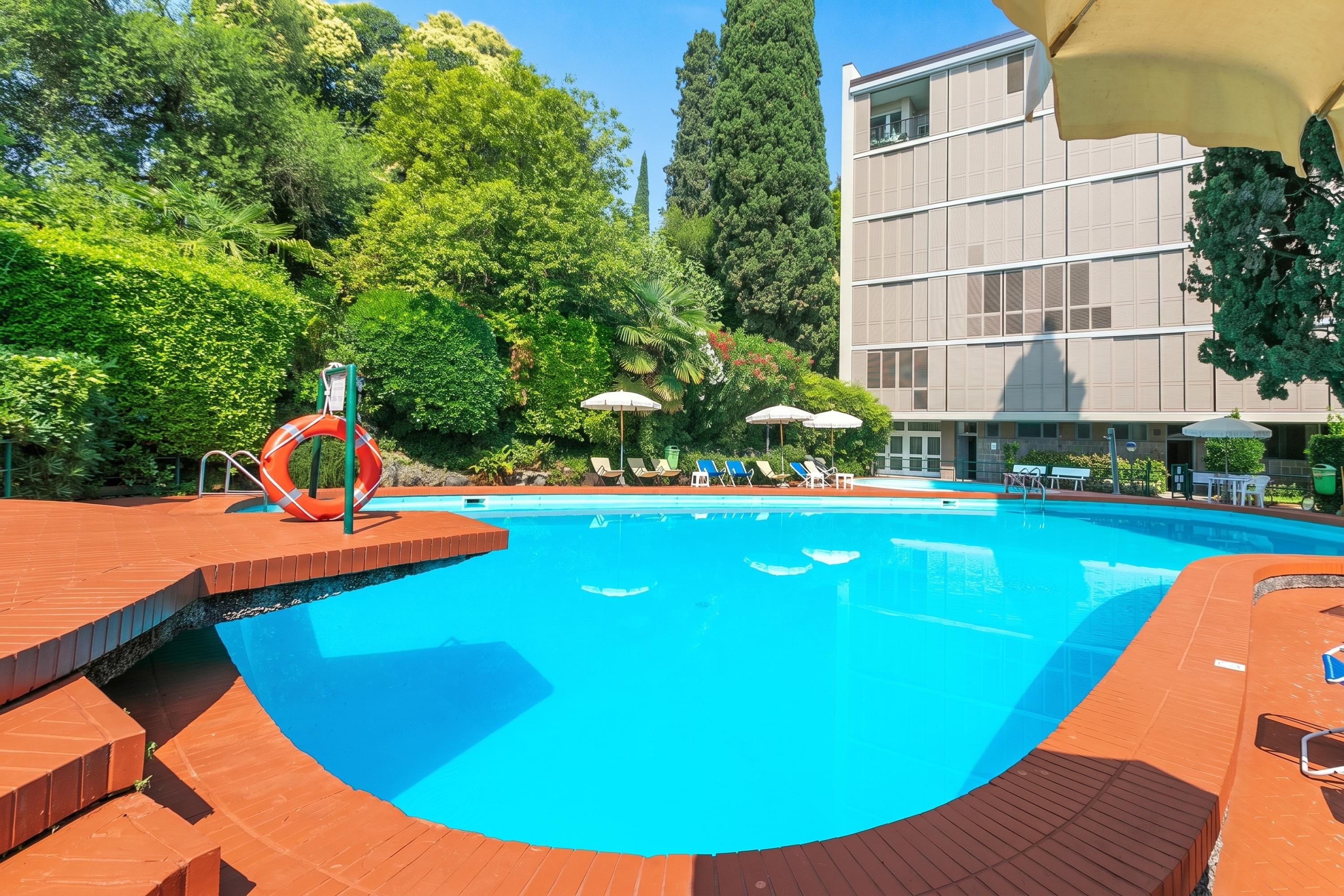 A swimming pool with a slide, surrounded by greenery and a building.