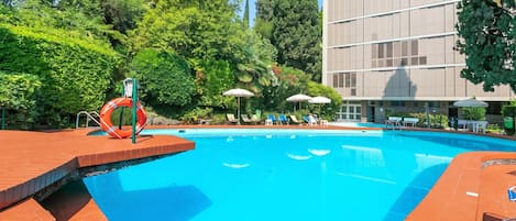 Piscina con tobogán, rodeada de vegetación y un edificio.