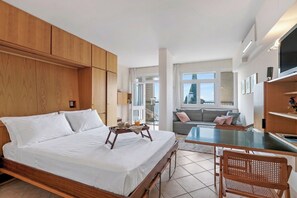 Quarto de hotel com uma cama grande, uma mesinha com bandeja, um sofá e uma televisão.