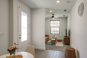 Un couloir bien éclairé, avec une porte, une fenêtre, un ventilateur de plafond et un téléviseur posé sur un meuble en bois.