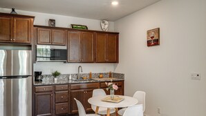 A modern kitchen with wooden cabinets, a stainless steel refrigerator, a granite countertop, and a dining area with white chairs. - 1BR Guest House w/ Private Entrance and Laundry (Bakersfield)