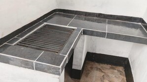 Esquina de una habitación con suelo de baldosas blanco y negro, un desagüe negro y una pared blanca.